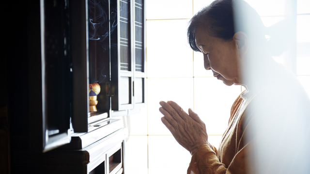 自宅の仏壇に手を合わせているシニア女性の姿
